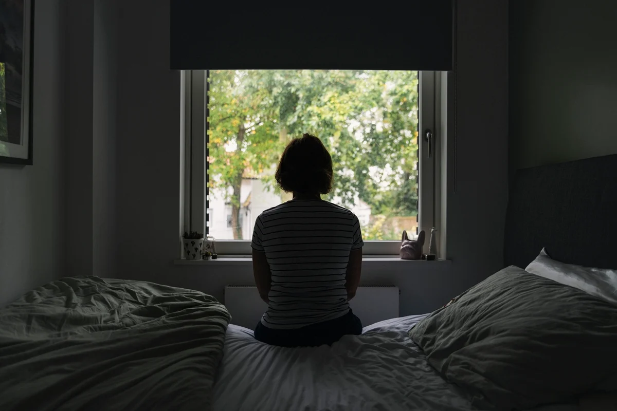 Imagem de uma mulher olhando pela janela do quarto - Psiquiatra explica o que é e como tratar depressão funcional - Metrópoles